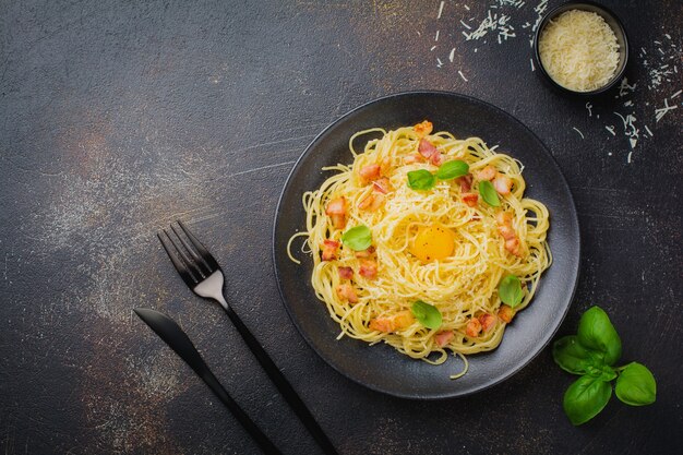 Pâtes spaghetti carbonara avec bacon, parmesan, jaune d'oeuf et feuilles de basilic sur une surface noire. Plat italien traditionnel