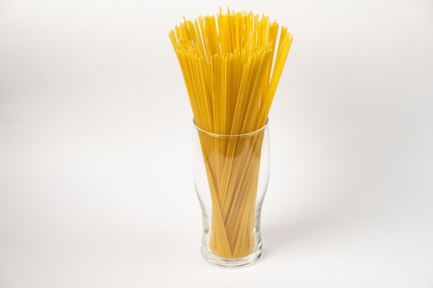 Pâtes spaghetti crues dans un verre isolé sur fond blanc