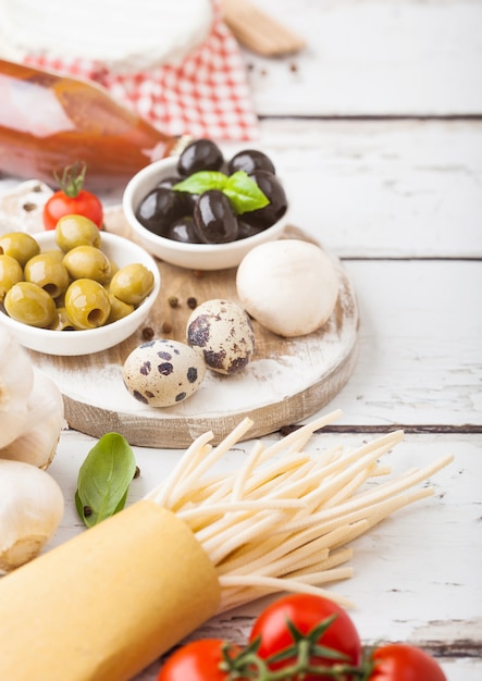 Pâtes spaghetti maison aux oeufs de caille avec bouteille de sauce tomate et fromage sur table en bois. Cuisine de village italienne classique. Ail, champignons, olives noires et vertes