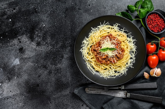 Pâtes spaghettis à la bolognaise avec tomate et viande hachée, parmesan et basilic. Fond noir