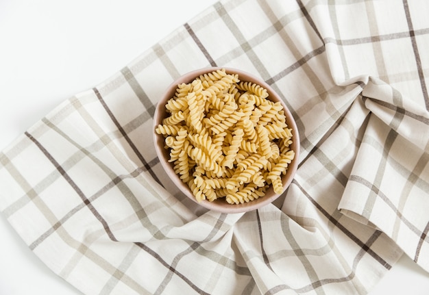 Pâtes en spirale non cuites dans l'assiette en céramique. mur de nappe à carreaux. vue de dessus