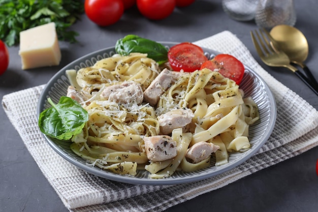 Pâtes tagliatelles au poulet et fromage servies avec tomates cerises et basilic sur fond gris