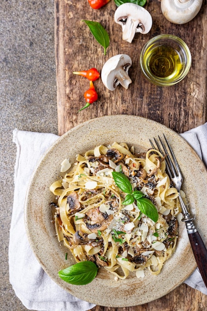 Pâtes tagliatelles aux champignons fromage et feuille de basilic sur la vue de dessus de plaque