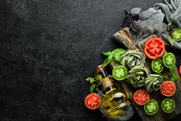 Pâtes vertes crues avec huile de tomates et persil sur fond de pierre noire Cuisine traditionnelle italienne Légumes frais Vue de dessus Espace libre pour votre texte