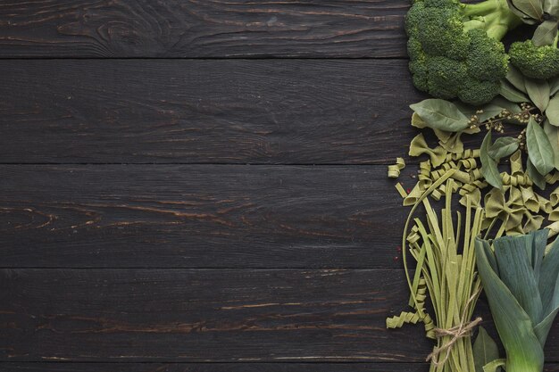 Pâtes vertes et légumes sur bois rustique. Cadre de macaroni, brocoli, feuilles de poireau et de laurier naturellement colorés, vue de dessus, espace de copie