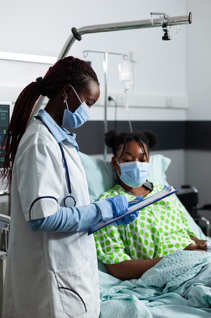 Patient afro-américain assis dans son lit pendant que le médecin vérifie les soins de santé