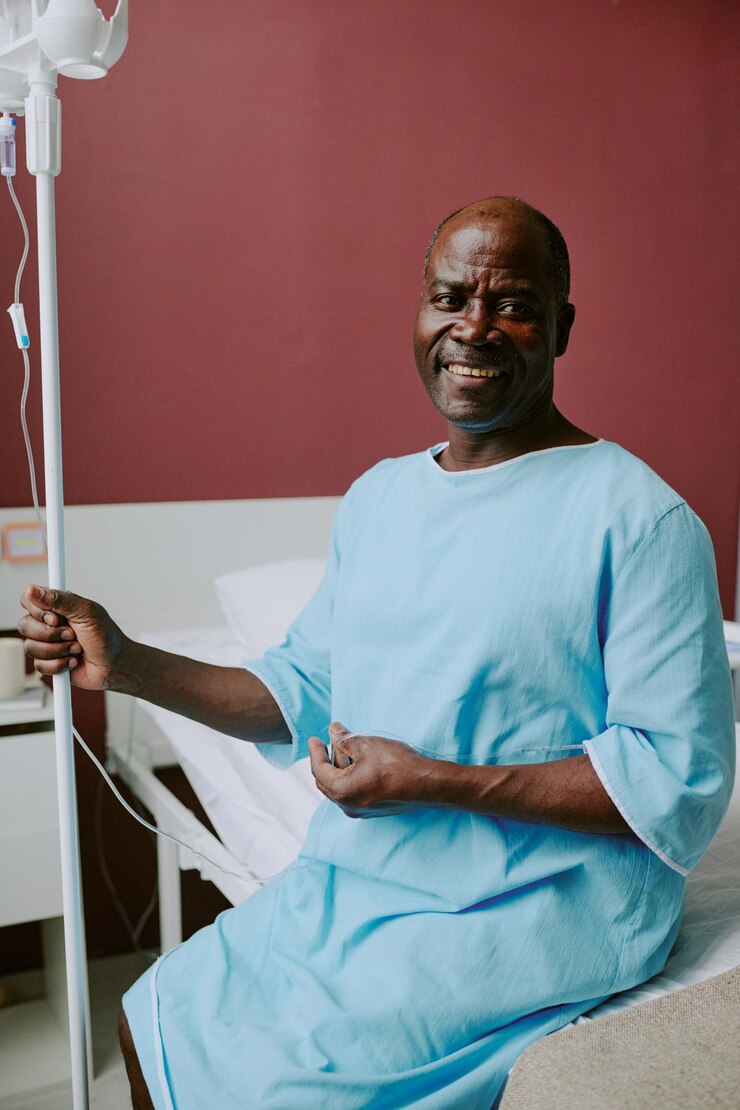 Photo patient afro-américain souriant assis sur un lit d'hôpital tenant une iv debout avec l'arrière-plan de la pièce