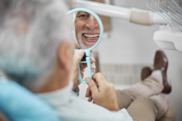 Patient âgé assis dans un fauteuil dentaire tout en se regardant dans le miroir