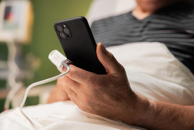 Un patient âgé en gros plan tenant un téléphone portable et un moniteur d'oxygène au bout du doigt