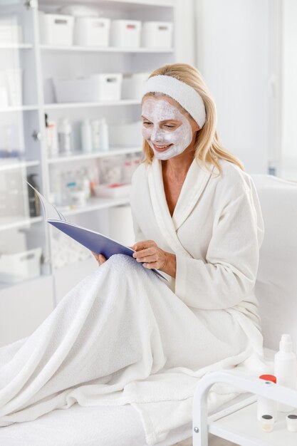 Le patient allongé sur le canapé attend les résultats du traitement de soins de la peau tout en lisant le catalogue.