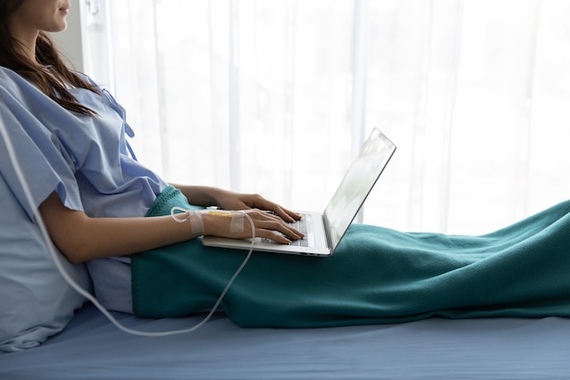 Photo patient asiatique femme couchée dans un lit d'hôpital à l'aide d'un ordinateur portable
