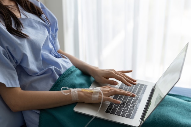 Photo patient asiatique femme couchée dans un lit d'hôpital à l'aide d'un ordinateur portable