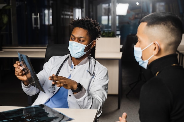 Photo patient asiatique lors d'un rendez-vous avec un médecin africain fracture des os du pied chirurgien noir montrant une radiographie au patient