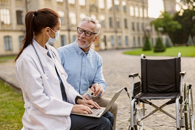 Patient en convalescence mature et joyeux avec un fauteuil roulant ayant une conversation avec une jeune femme médecin