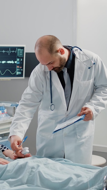 Patient malade discutant de la maladie et du traitement avec un médecin en salle d'hôpital. Femme à la retraite avec tube d'oxygène nasal et sac de perfusion IV parlant à un médecin lors d'une visite de contrôle pendant que l'infirmière apporte son soutien