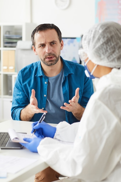 Patient mature assis à la table et discutant de sa maladie et des moyens de traitement avec le médecin au bureau