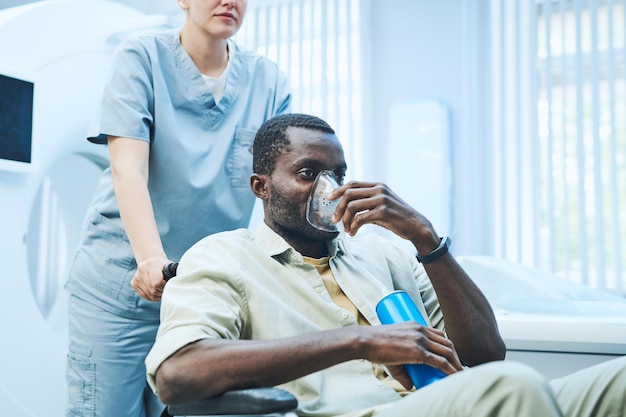 Patient noir fatigué ayant un manque d'oxygène assis dans une chaise roulante poussé par une infirmière et respirant avec un masque à oxygène