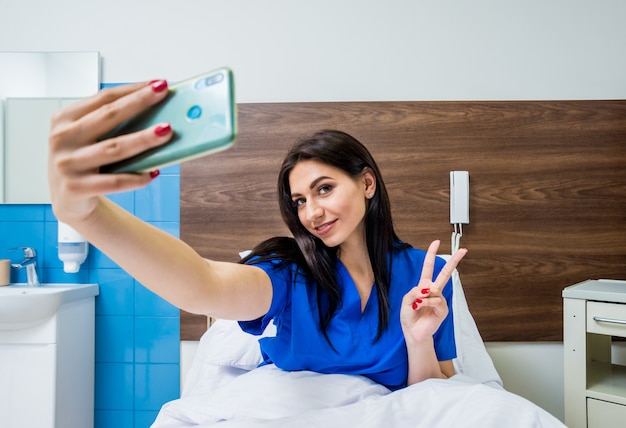 Patient parlant sur téléphone mobile dans un lit d'hôpital. Jeune femme caucasienne.