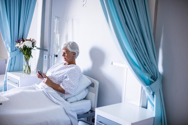 Patient senior féminin à l'aide de téléphone portable sur le lit