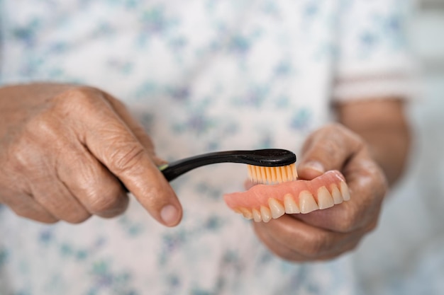 Une patiente âgée asiatique utilise une brosse à dents pour nettoyer la prothèse partielle des dents de remplacement