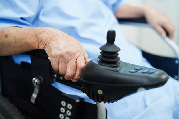 Patiente âgée handicapée asiatique utilise un fauteuil roulant électrique à joystick à l'hôpital