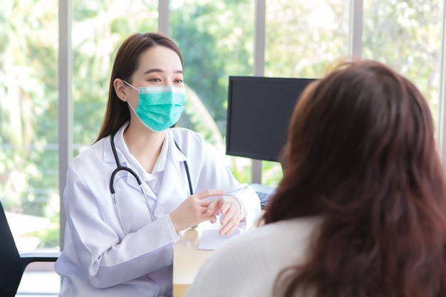 Une patiente asiatique âgée est contrôlée par un médecin tandis que les deux portent un masque facial à l'hôpital