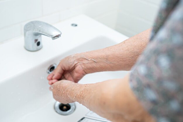 Patiente asiatique senior se laver les mains dans les toilettes.