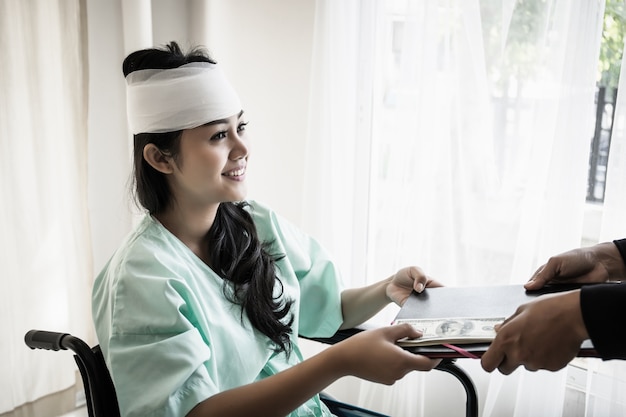 Patiente assise dans une infirmière en fauteuil roulant donnant ses documents dans sa main. Concept de blessure et de guérison.