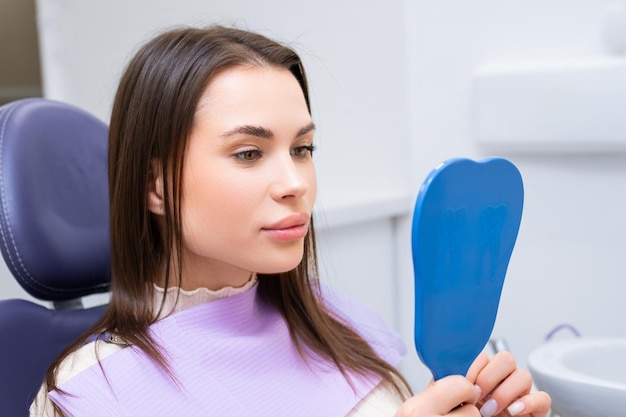 Une patiente brune se regarde dans le miroir dans la clinique dentaire après un examen.