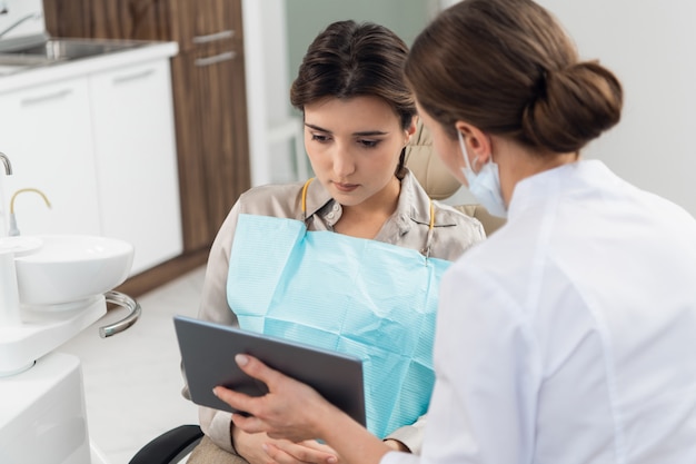 Une patiente avec un médecin à l'aide d'une tablette dans une clinique dentaire