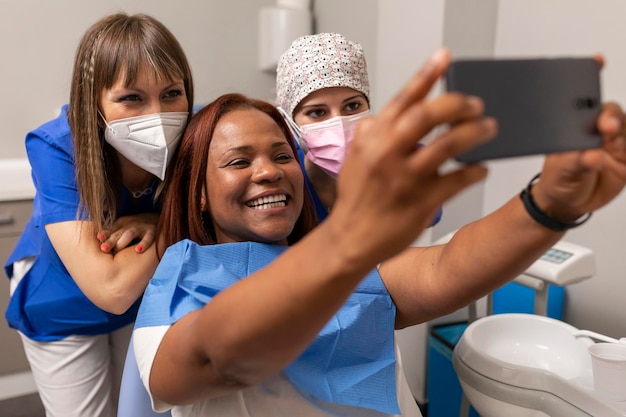 Une patiente noire prend une photo de selfie heureuse avec le smartphone côte à côte le dentiste et l'hygiéniste dentaire à la clinique dentaire