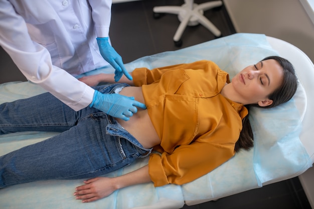 Patiente Portant Sur Un Canapé Dans Le Bureau Du Médecin Pendant Que Le Médecin Palpe Son Estomac