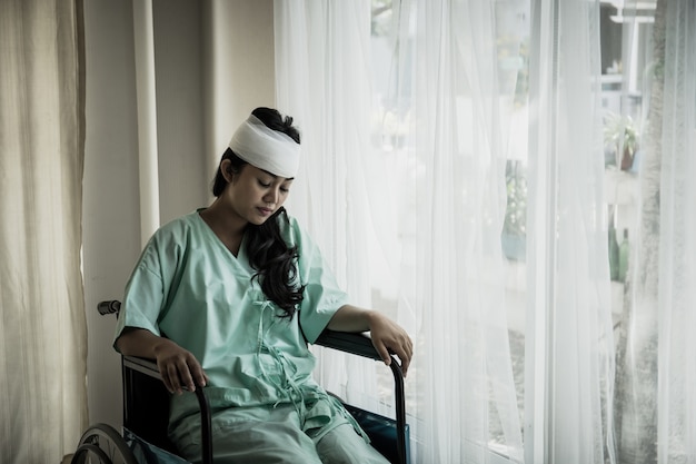 Patientes ayant des douleurs dans la tête après une hospitalisation assis sur un fauteuil roulant dans la chambre du patient