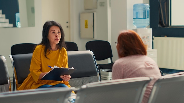 Patients asiatiques remplissant des dossiers de rapport de contrôle au centre de santé, parlant du soutien de l'assurance maladie et rédigeant un formulaire médical. Avoir un rendez-vous de consultation avec un médecin dans l'établissement.