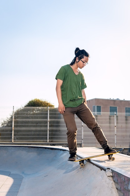 Patineur asiatique monté sur un skatebard au skatepark au coucher du soleil