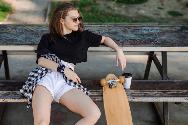 Une patineuse adolescente avec une planche à roulettes se détend sur le banc du parc des patineurs