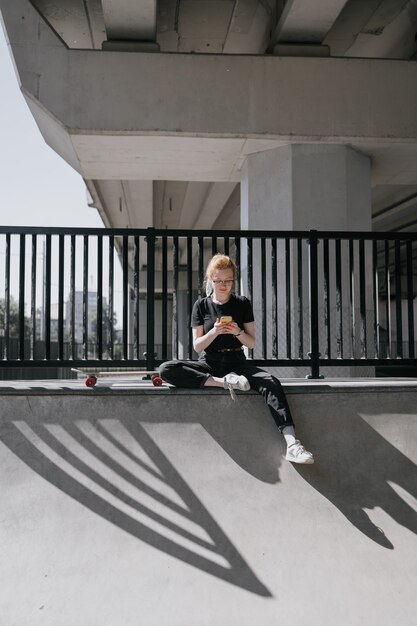 Une patineuse européenne aux cheveux rouges monte une planche à roulettes sur un patin à roulettes une femme en noir