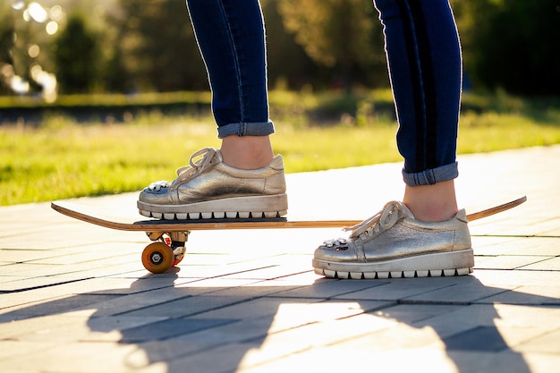 Patineuse de fille dans un parc d'été. jambes pieds de femme en jeans à la mode et baskets élégantes sur un asphalte de longboard de skateboard. concept de skateboard pour les jeunes.