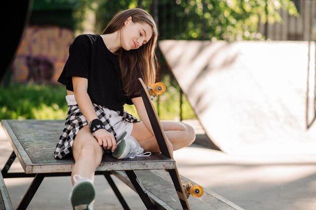 Une patineuse avec une planche à roulettes est assise et se repose dans le parc des patineurs