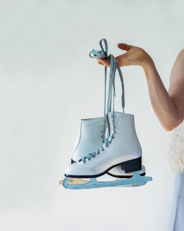 Photo patins artistiques blancs classiques en cuir femme élégante vêtue de la robe grise et du gilet de fausse fourrure tient des chaussures en dentelle de patinage sur glace dans sa main isolée sur le fond blanc espace de copie
