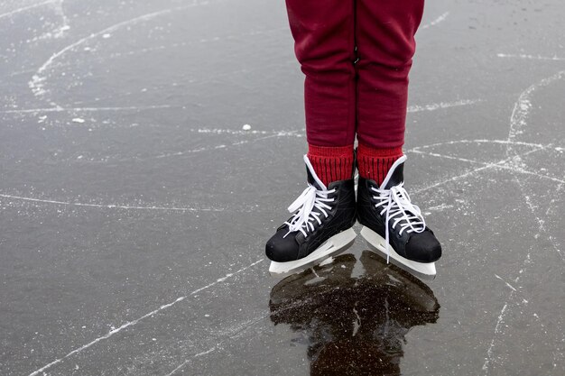 Patins noirs sur glace Les jambes des femmes en pantalon bordeaux se tiennent à la surface d'un lac de forêt gelé