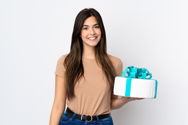 Pâtissier adolescent tenant un gros gâteau sur un mur blanc isolé souriant beaucoup