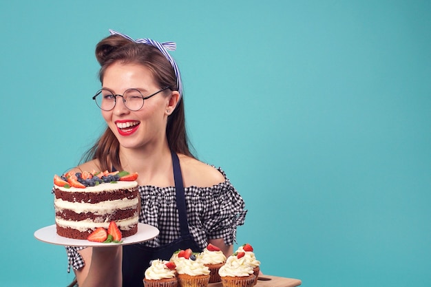 Pâtissier brune émotionnelle tenant un gâteau sur sa paume et souriant à la caméra dans le Studio