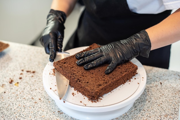 Pâtissier cuisinier pâtissier ou boulanger en gants noirs et tablier de cuisine noir fait un gâteau. Gâteau d'anniversaire fait maison. Concept de pâtisserie maison, cuisson de gâteaux, passe-temps. Petite entreprise à domicile féminine.