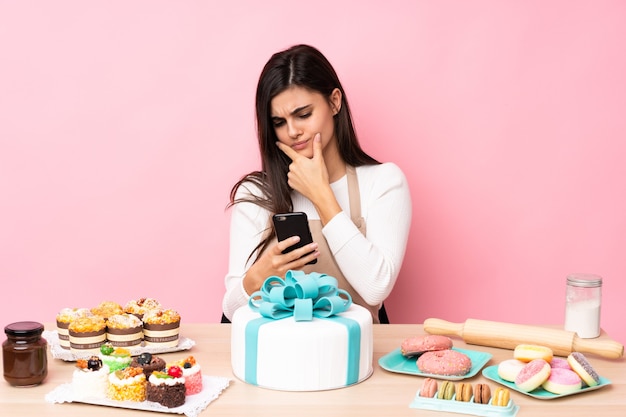 Pâtissier avec un gros gâteau dans une table sur la pensée rose isolé et l'envoi d'un message