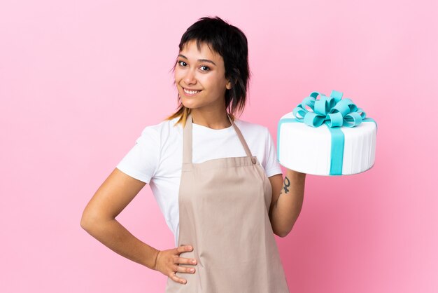 Pâtissier uruguayen tenant un gros gâteau sur le mur rose applaudissant