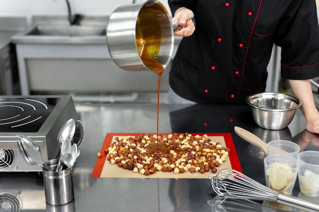 Le pâtissier verse du sirop chaud, du caramel sur des noisettes pour faire du praliné