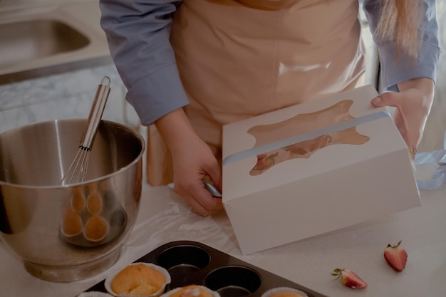 Une pâtissière met des cupcakes dans un emballage pour les expédier aux clients présentant des gâteaux faits maison.