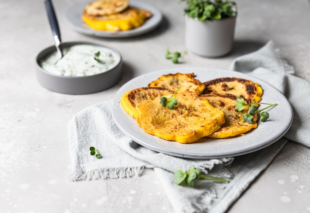 Pâtisson frit ou courgette jaune avec sauce et micro greens, fond de béton gris.