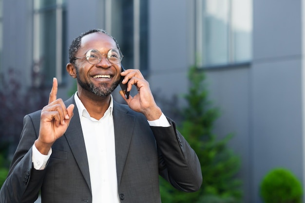 Patron afro-américain joyeux et satisfait à l'extérieur de l'immeuble de bureaux souriant et parlant à